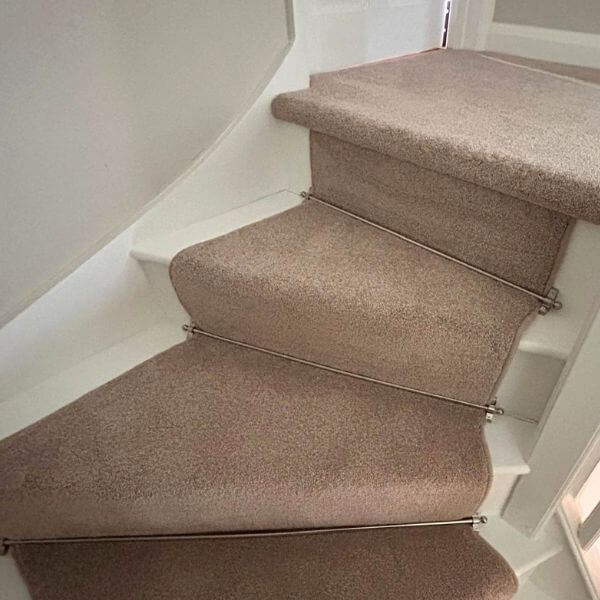 Beige coloured carpet fitted on stairs with corner, with nickle stair rods