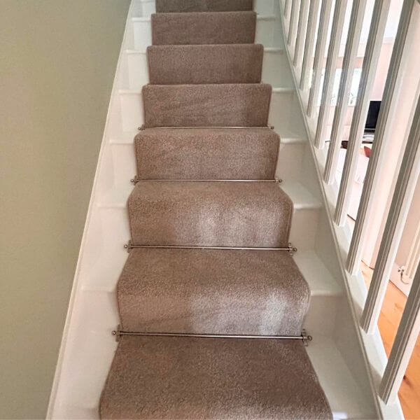 Beige coloured carpet fitted on stairs, with nickle stair rods